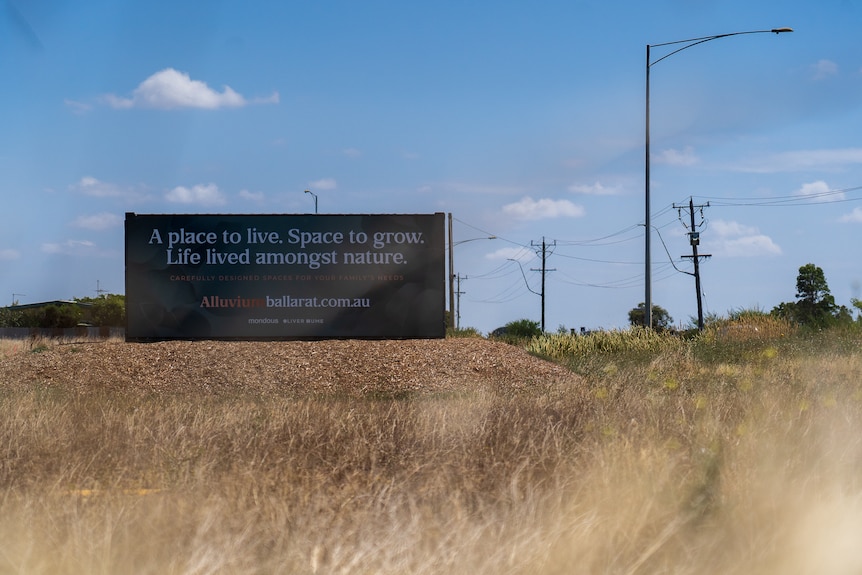 A billboard in a paddock saying 'a place to live. Space to grow.Life lived amongst nature'.
