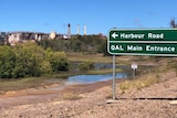 Harbour Road, QAL Main Entrance sign, alumina refinery in background, blue sky, green swamp land in foreground.