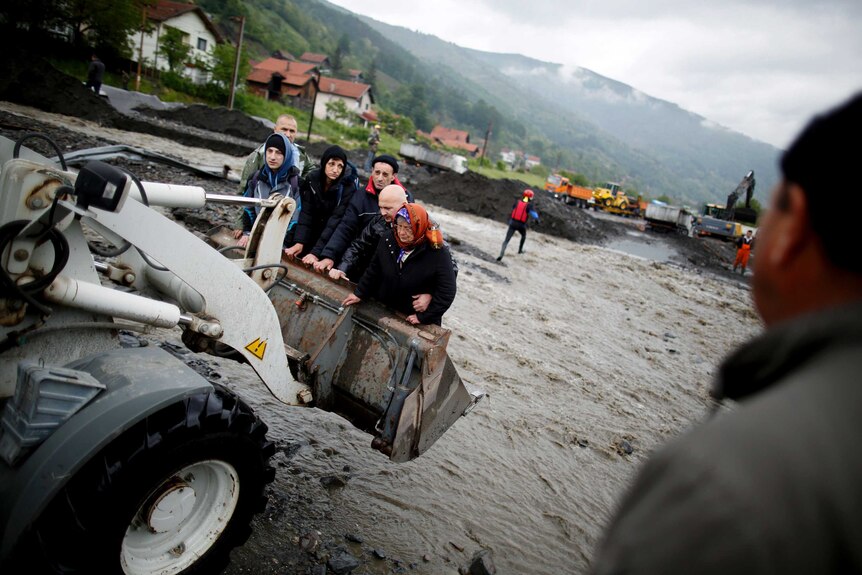 People are carried by a front loader as they evacuate from their flooded houses in Bosnia