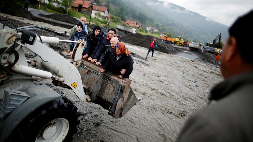 People are carried by a front loader as they evacuate from their flooded houses in Bosnia