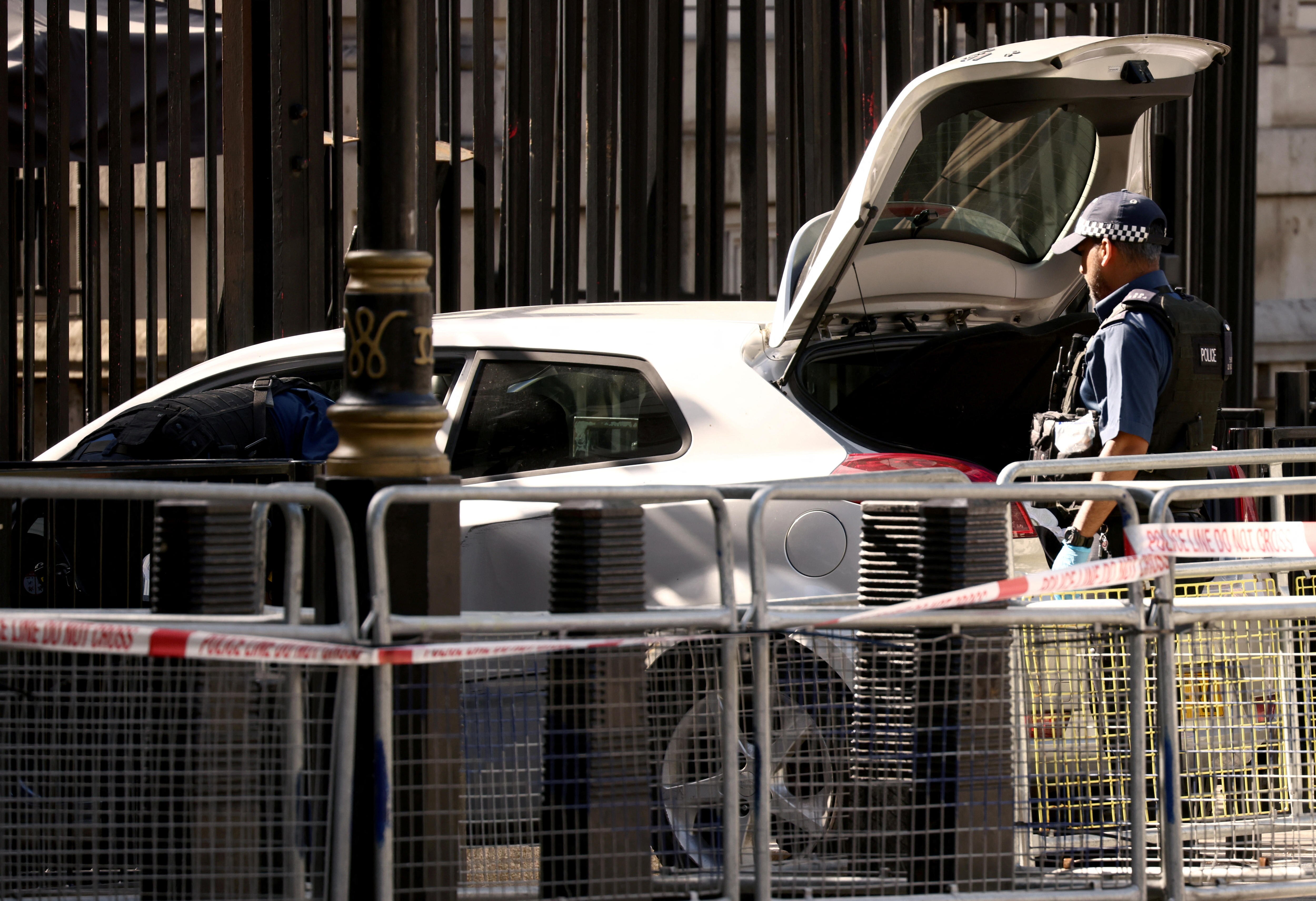 A police officer inspects the open boot of a white hatchback.