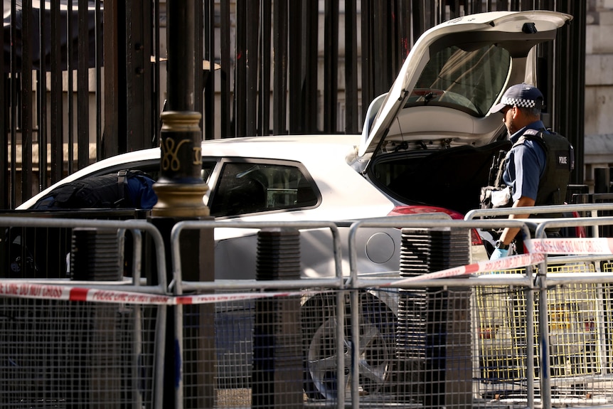A police officer inspects the open boot of a white hatchback.