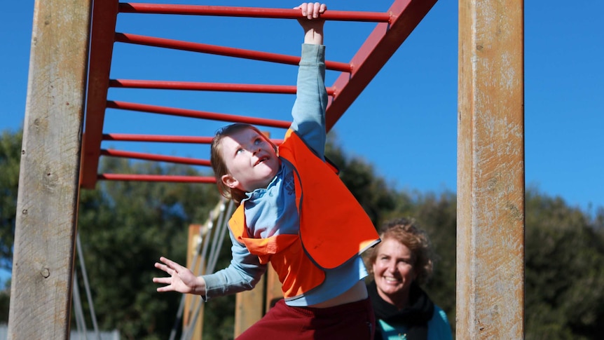 Child in high-vis vest on monkey bars with adult watching