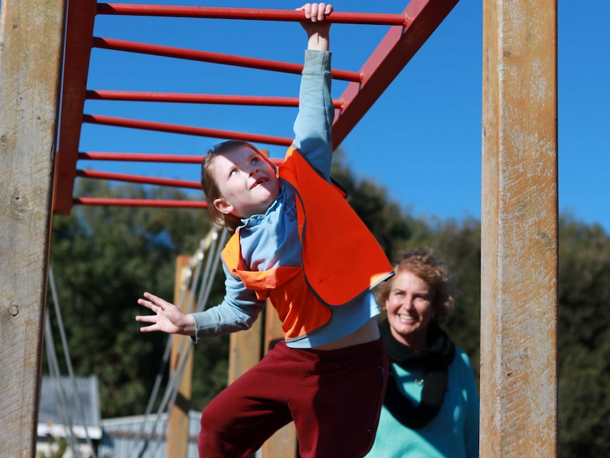 Child in high-vis vest on monkey bars with adult watching