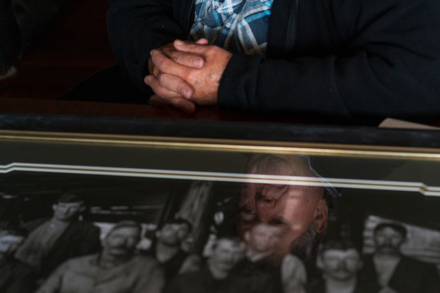 The reflection of a man in a photo of his ancestors, who were loggers. 