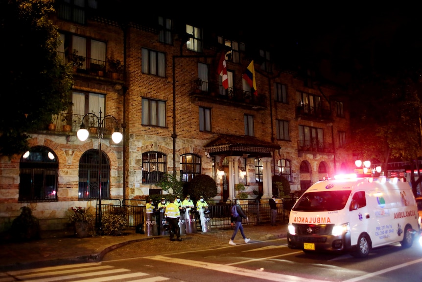 At night, a flurry of activity including police and an ambulance outside a tall brick building