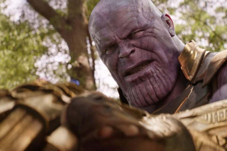 Purple-faced Thanos looks own at his golden gauntlet covered in infinity stones.