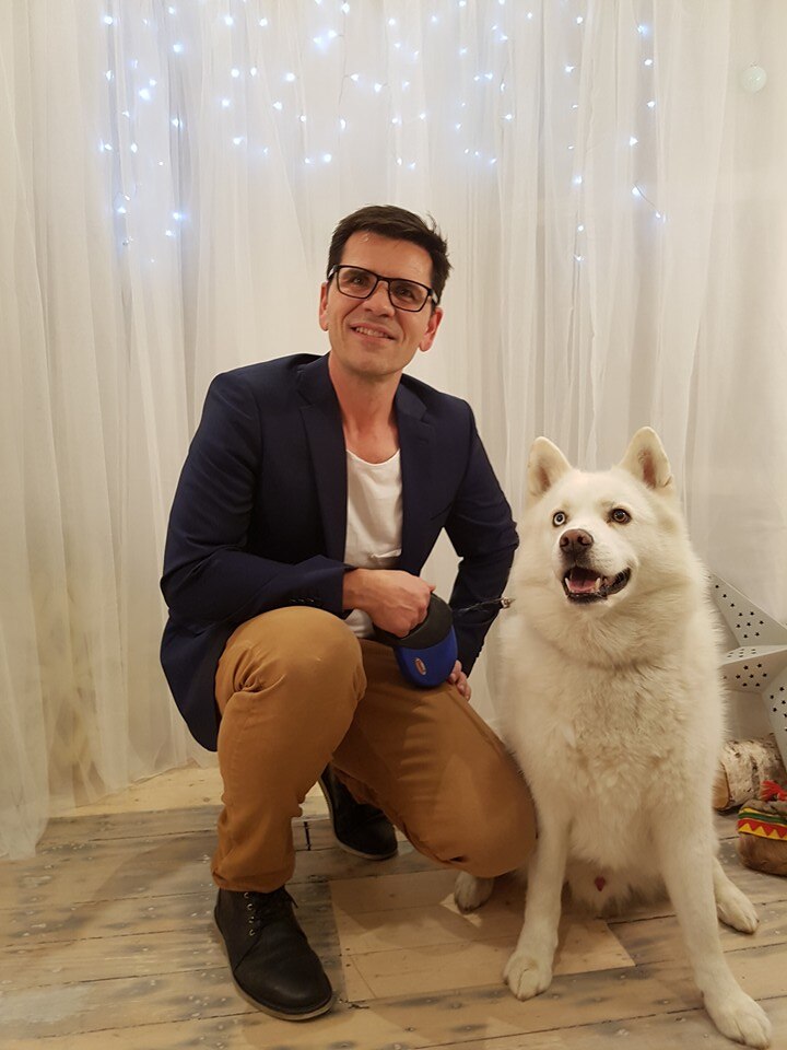 Hombre sonriente con chaqueta con perro blanco.
