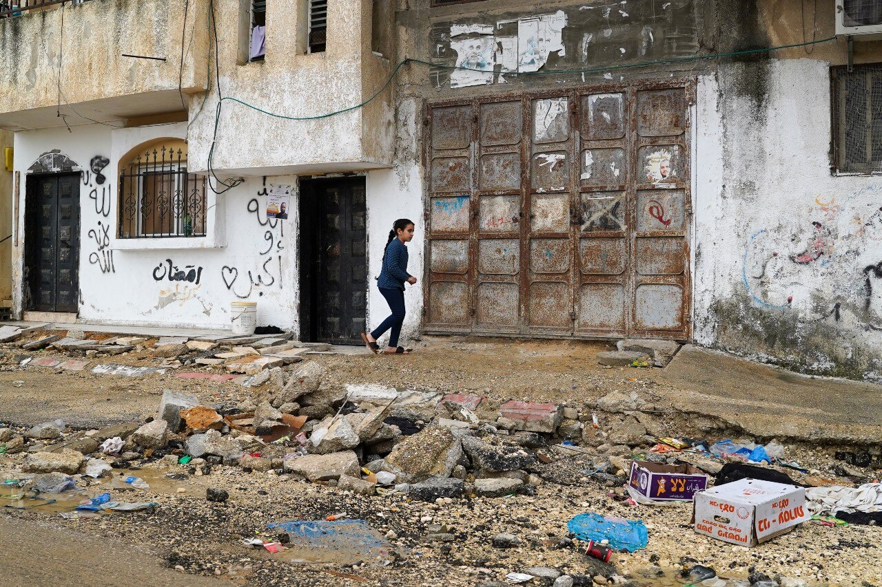 A young girl, seen from a distance, walking on a damaged street.