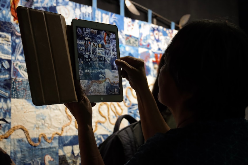 A lady taking a photo of a quilt with an ipad.