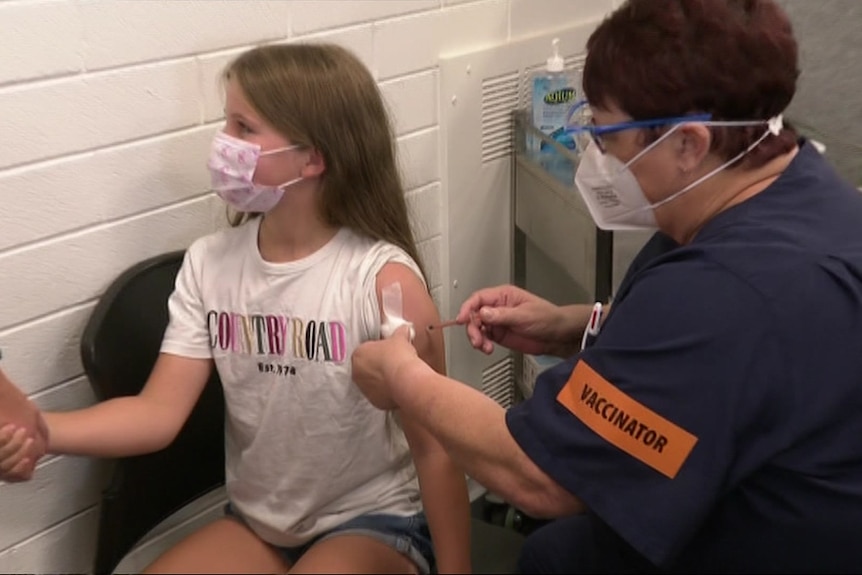 A 10-year-old girl gets a vaccination in her arm from a nurse