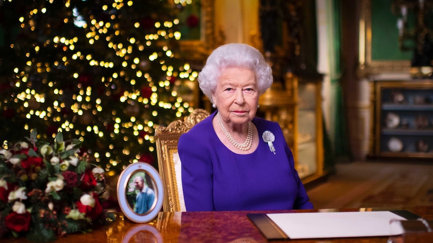 Britain's Queen Elizabeth sits behind a desk next to a photo of her husband.