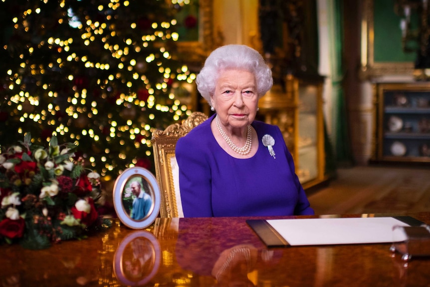 Britain's Queen Elizabeth sits behind a desk next to a photo of her husband.