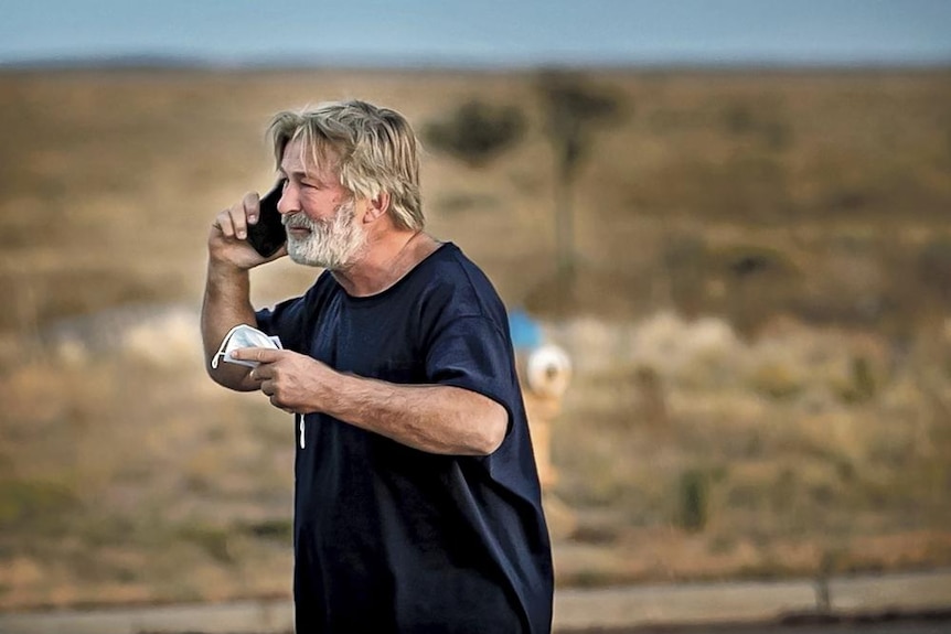 Ein Mann mit graubraunem Haar und Bart telefoniert in einer einsamen, trockenen Landschaft 