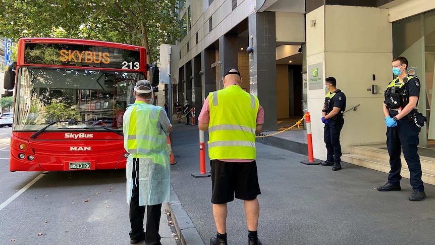 A large red bus outside an inner city hotel, with two police officers and and two people in high-vis standing out the front.