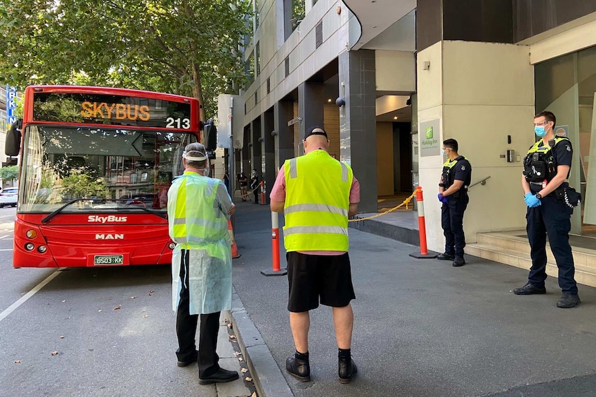 A large red bus outside an inner city hotel, with two police officers and and two people in high-vis standing out the front.