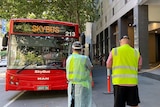 A large red bus outside an inner city hotel, with two police officers and and two people in high-vis standing out the front.