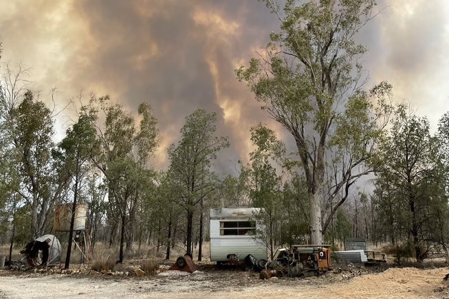 A caravan in the bush, near where a fire is burning.