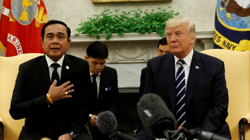 Thai PM Prayut Chan-o-cha holds his hand on his chest as he talks. US President Donald Trump is sitting next to him