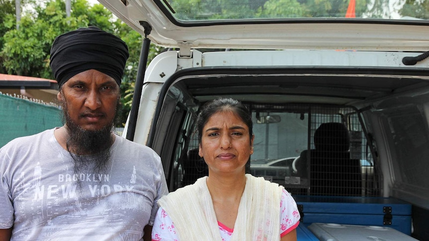 An Indian man and woman stand in front of an open van.