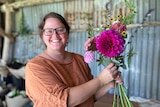a woman stands inside a shed holding a bunch of flowers