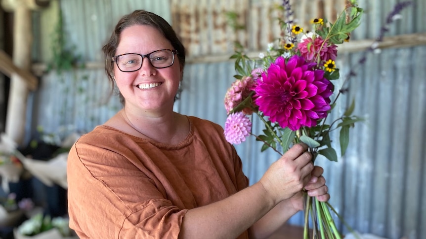 a woman stands inside a shed holding a bunch of flowers
