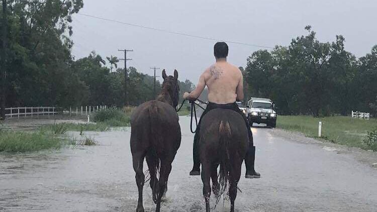 A man on a horse leading another horse through flooded water in Bluewater.