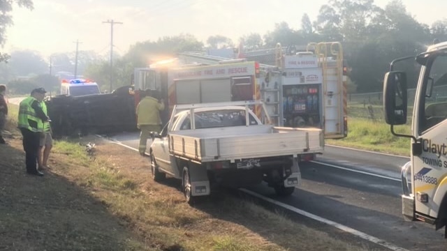 A car rolled on its side on the road near a fire truck and white ute