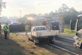 A car rolled on its side on the road near a fire truck and white ute