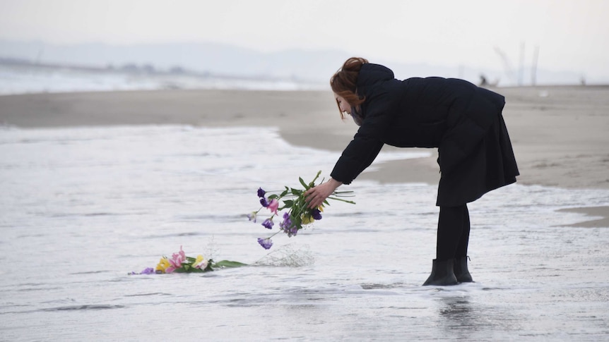 A woman places a bouquet into the sea