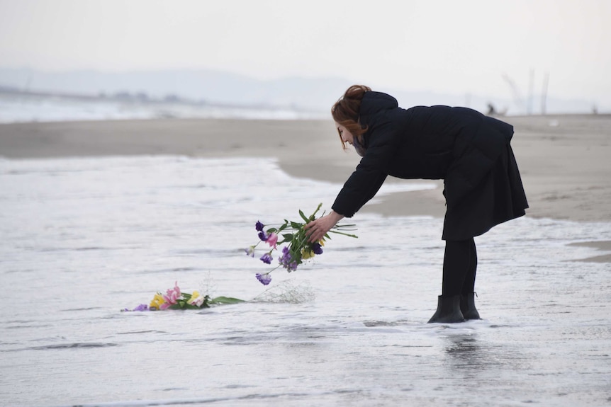 A woman places a bouquet into the sea