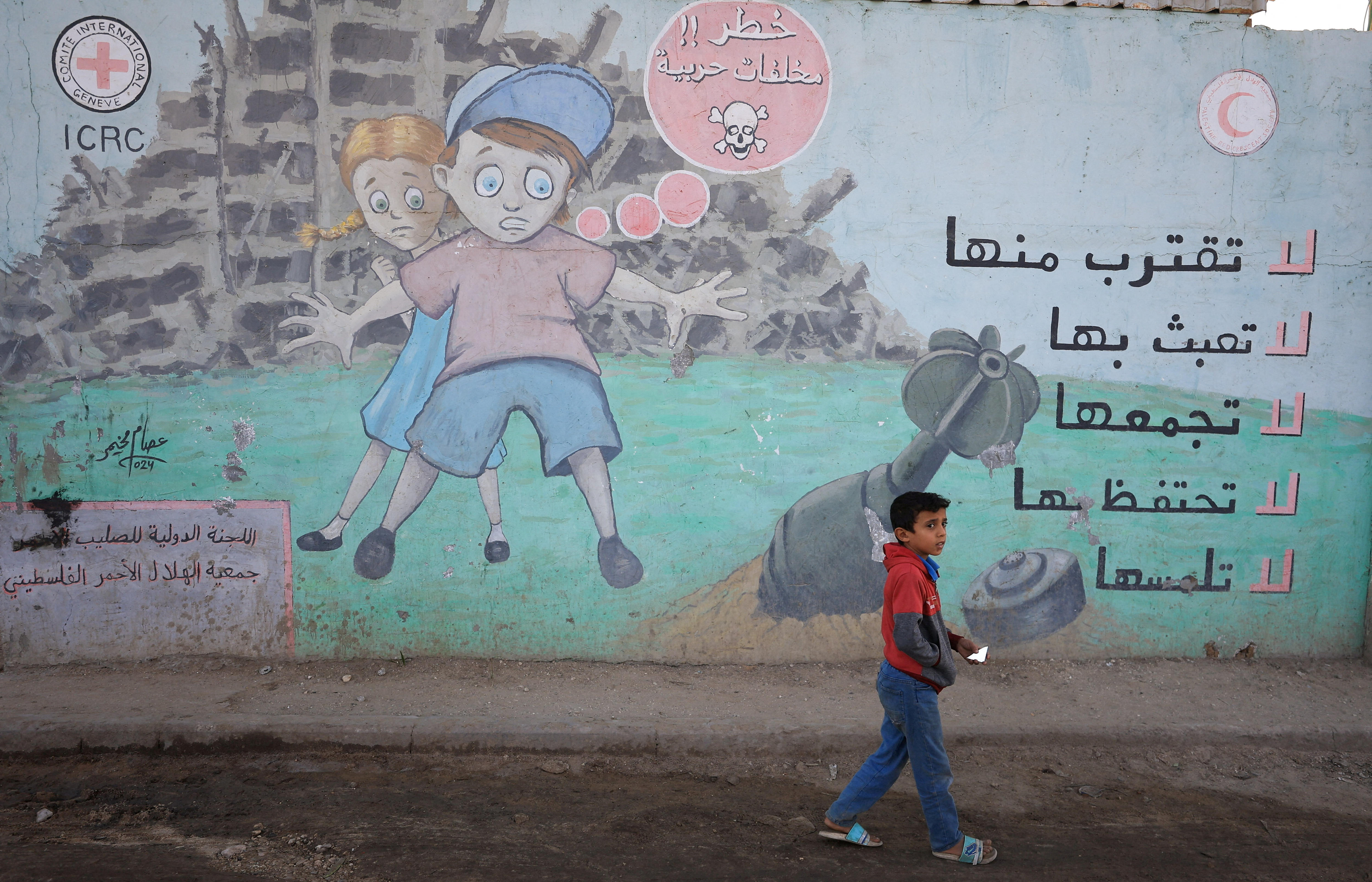 A Palestinian child walks past a mural warning against approaching unexploded ordnance.