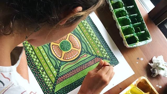 the back of a woman's head while she is dot painting a picture in in green and brown
