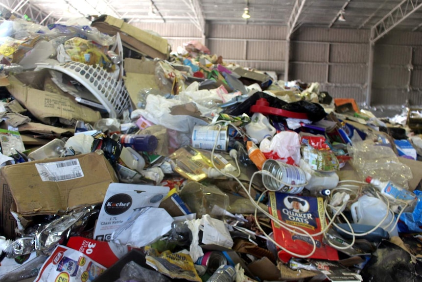 A mountain of unsorted recycling seen through a glass window at the Materials Recovery Facility.