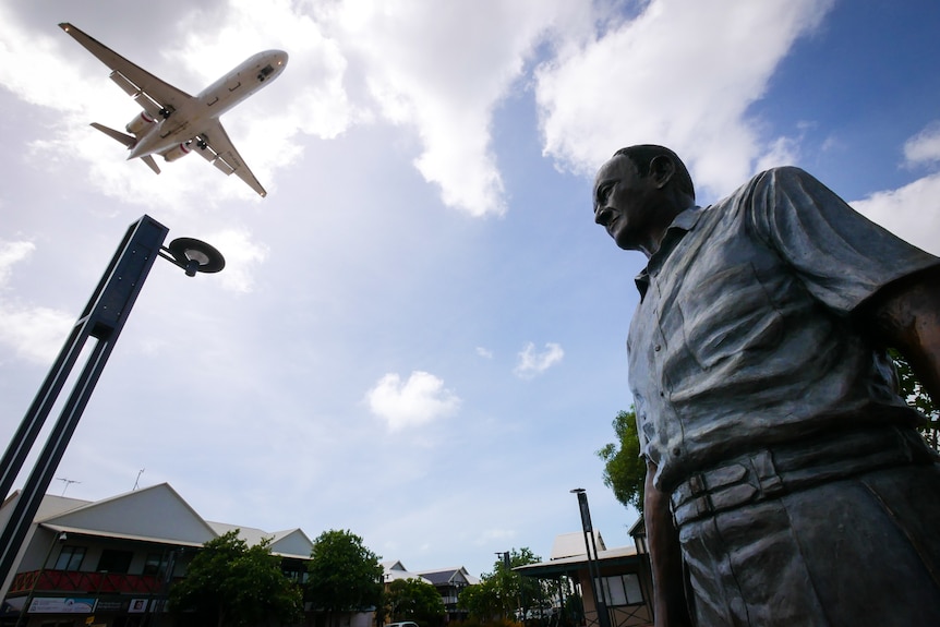 A plane flies over a statue of Sam Male in Broome's Chinatown