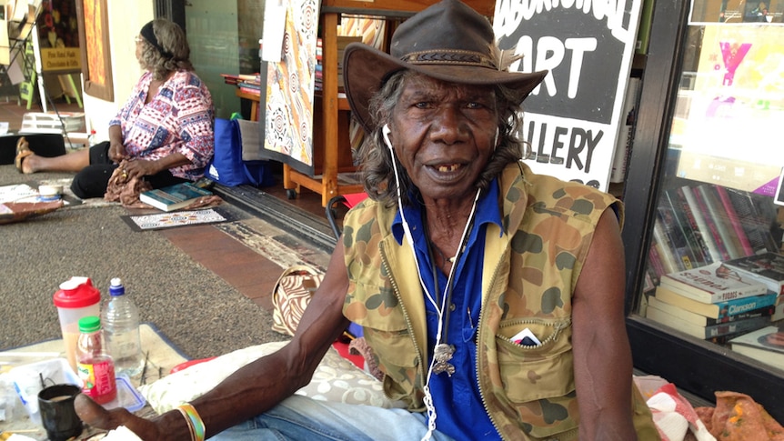 A profile photo of actor David Gulpilil sitting outside a book store at the Darwin mall with canvases and paints