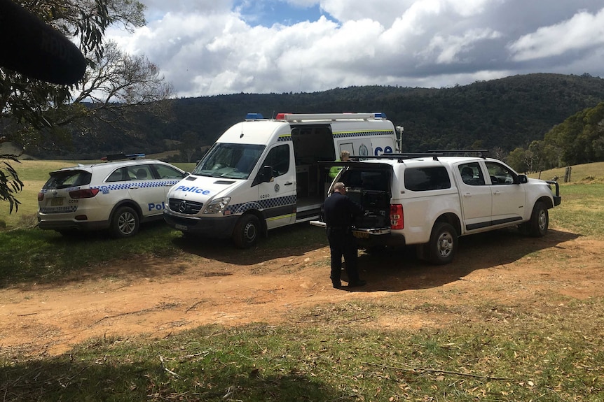 A man is seen standing at the back of a vehicle, with two police vehicles seen behind him.