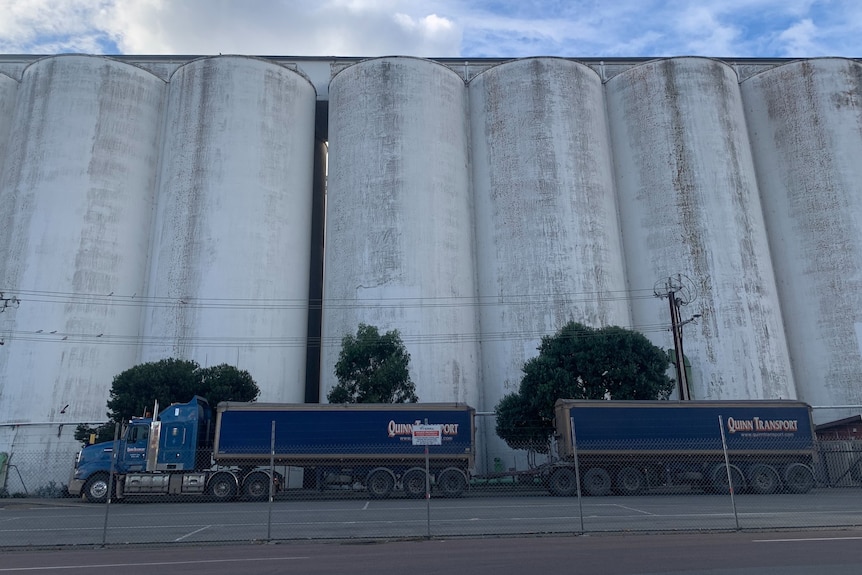 A blue truck in front of huge silos.