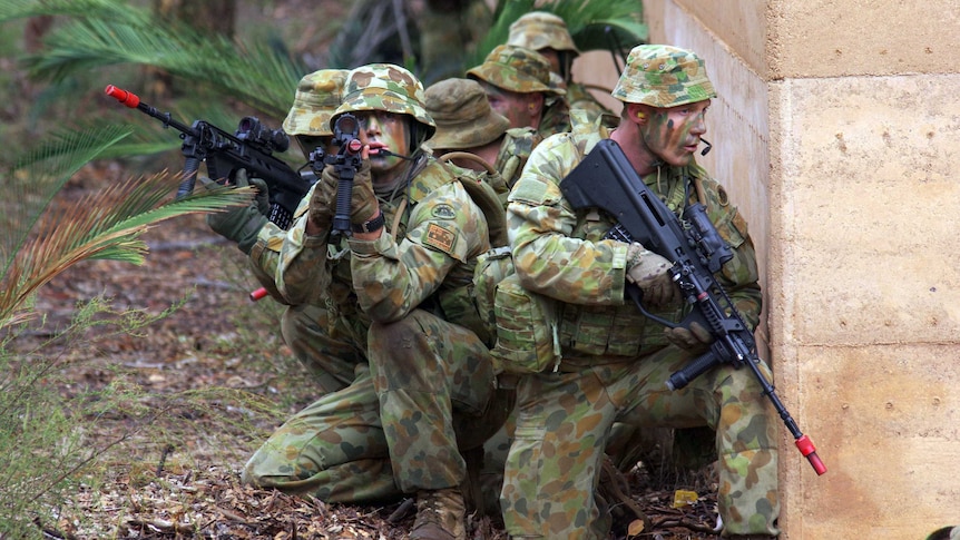 A group of Army Reservists with guns crouched down behind a wall.