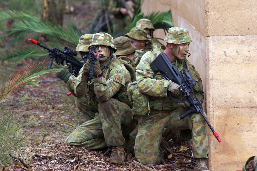 A group of Army Reservists with guns crouched down behind a wall.