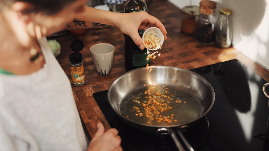 Photo from above a person's head as they pour seeds into a pan sitting on a flat, black induction cook top.