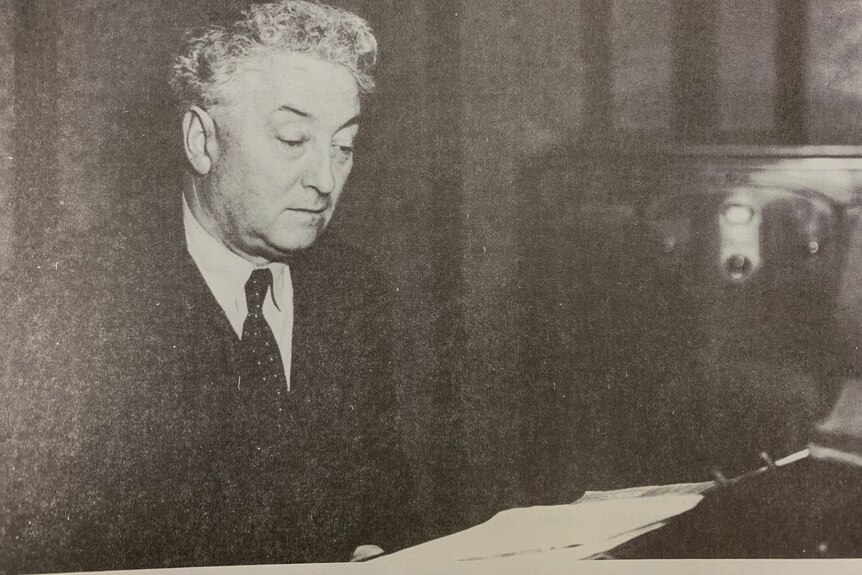Black and white photo of Prime Minister Lyons in a suit in a studio, reading off a piece of paper