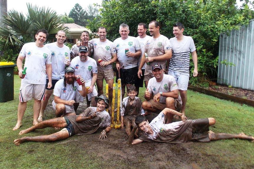 A group of cricketers in white on a muddy cricket pitch.