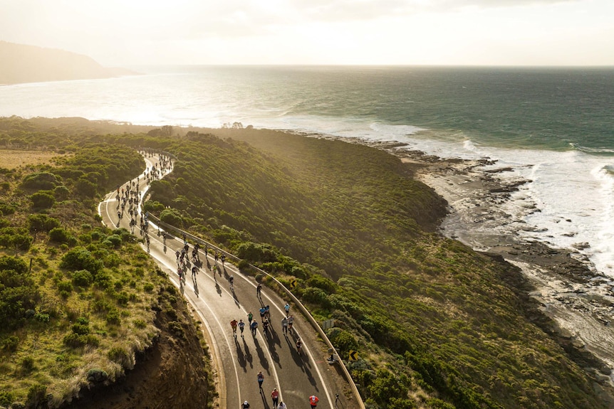 Aerial photo with people running along a winding road along the ocean without cars 