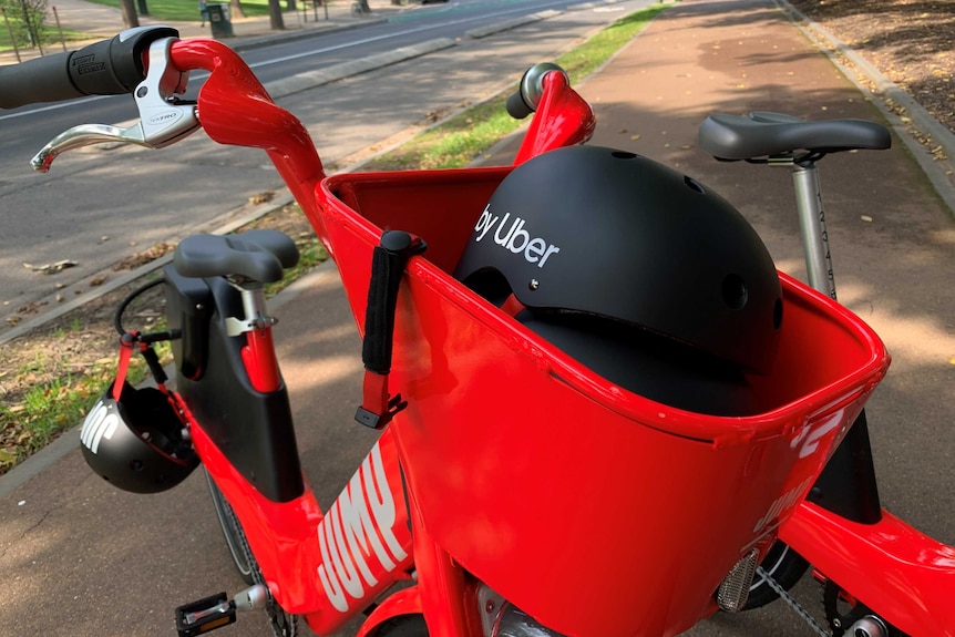 A red electric bike with a black helmet in the front basket and another one hanging from the back wheel.