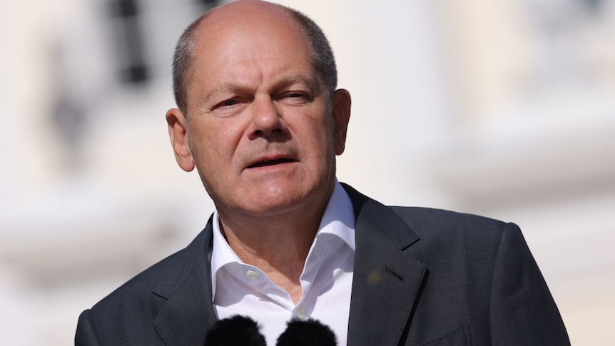 Olaf Scholz faces two microphones in a suit and unbuttoned white shirt
