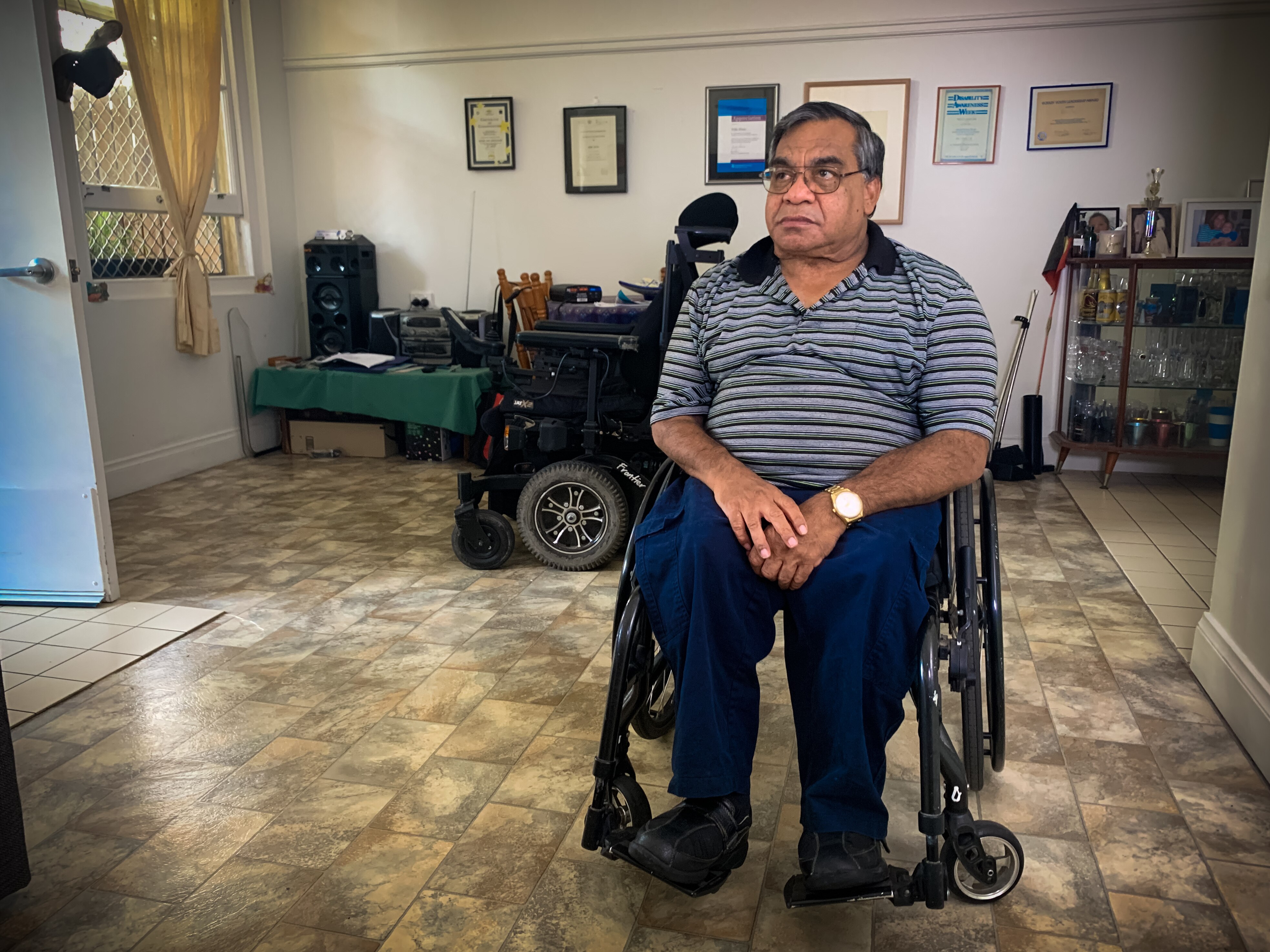 Um homem em uma cadeira de rodas na sala de sua casa olha para longe