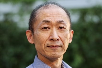A portrait image of a Japanese man in a blue collared shirt. 