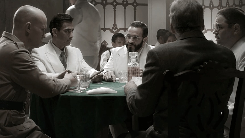 Well-dressed men in the 1930s talk at a poker table.