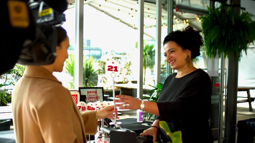 Woman wearing a black shirt stands behind a till in a Brodburger restaurant